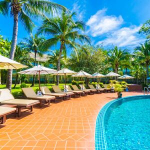 Beautiful luxury umbrella and chair around outdoor swimming pool in hotel and resort with coconut palm tree on blue sky - Boost up color Processing